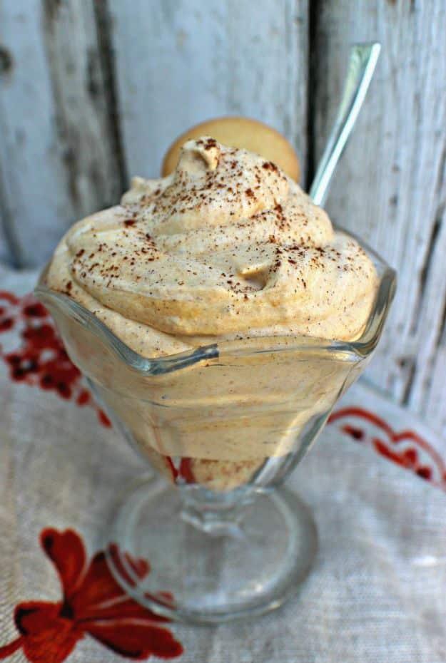 Tall glass dish of fluffy orange cheesecake mousse dusted with warm spice and topped with a small cookie