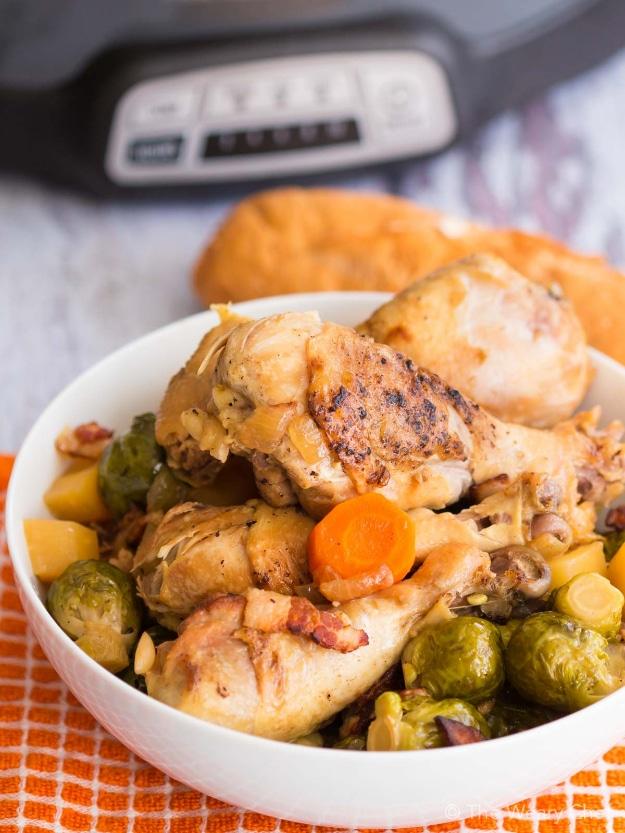 Cooked bone-in chicken over Brussels sprouts and carrots in a white bowl from a slow cooker recipe dish