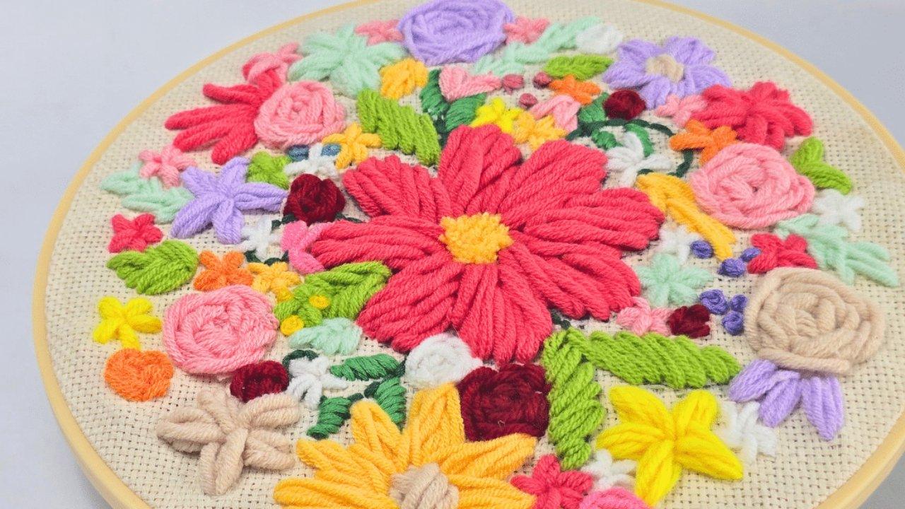 Close up of a punch needle hoop packed with thick yarn flowers in pink, yellow, coral and lilac on cream monks cloth