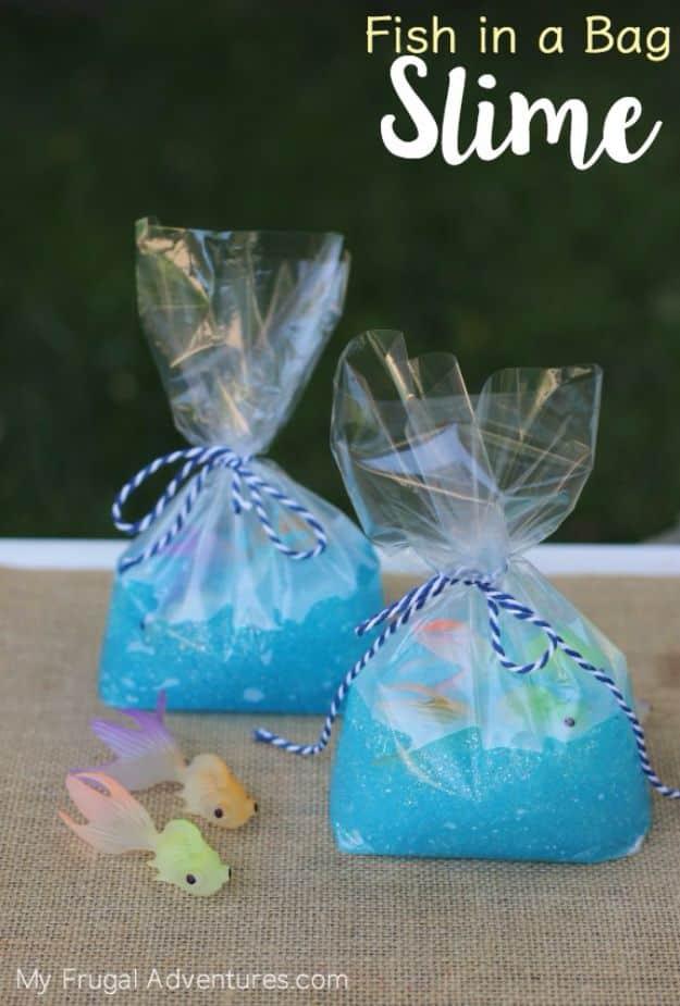 Two clear treat bags of blue glitter slime holding plastic goldfish, tied with navy twine, with two loose toy fish