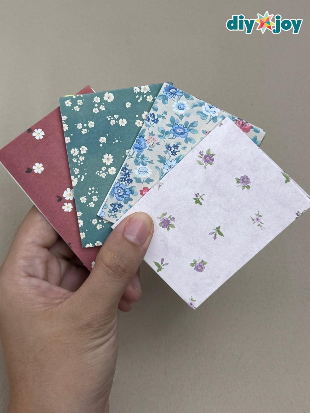 Small handmade notebooks with floral and solid cardstock covers held in one hand, one open to yellow accordion pages
