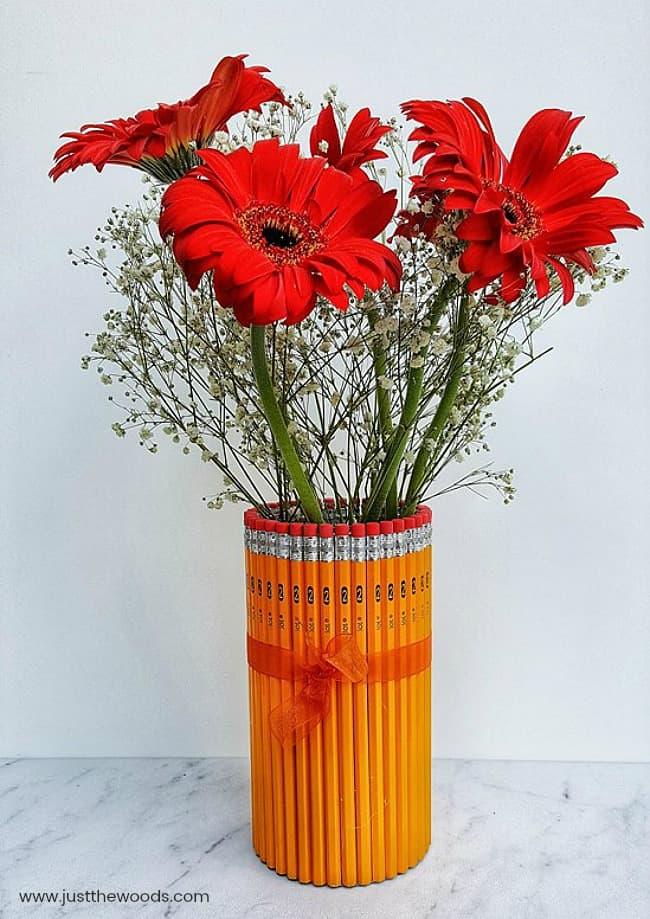 Glass vase wrapped in yellow pencils tied with an orange ribbon and filled with red gerbera daisy flowers