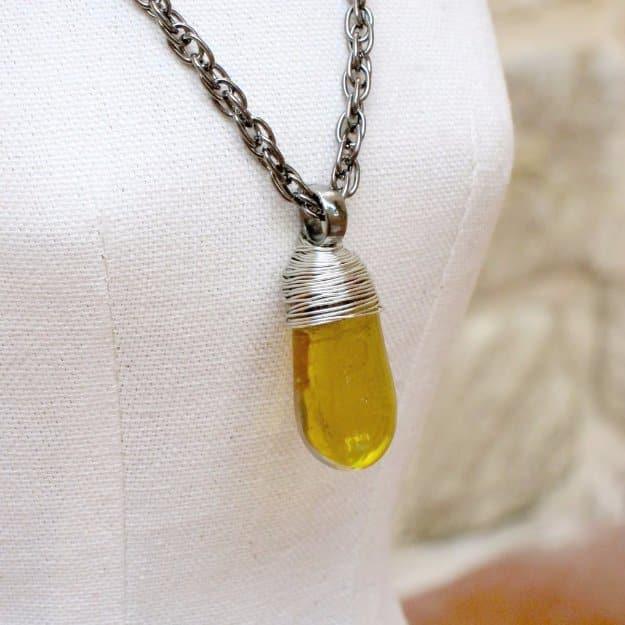 A flat glass marble caged in coiled copper wire and strung on a brown cord, lying on a pale linen cloth