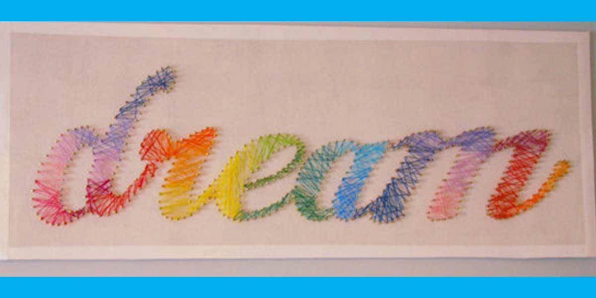 DREAM string art, the word dream in rainbow string wound around nails on a white board with blue edges