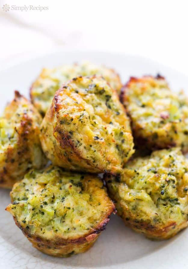 Broccoli cheddar egg bites piled on a white plate, small golden rounds flecked with broccoli and melted cheddar