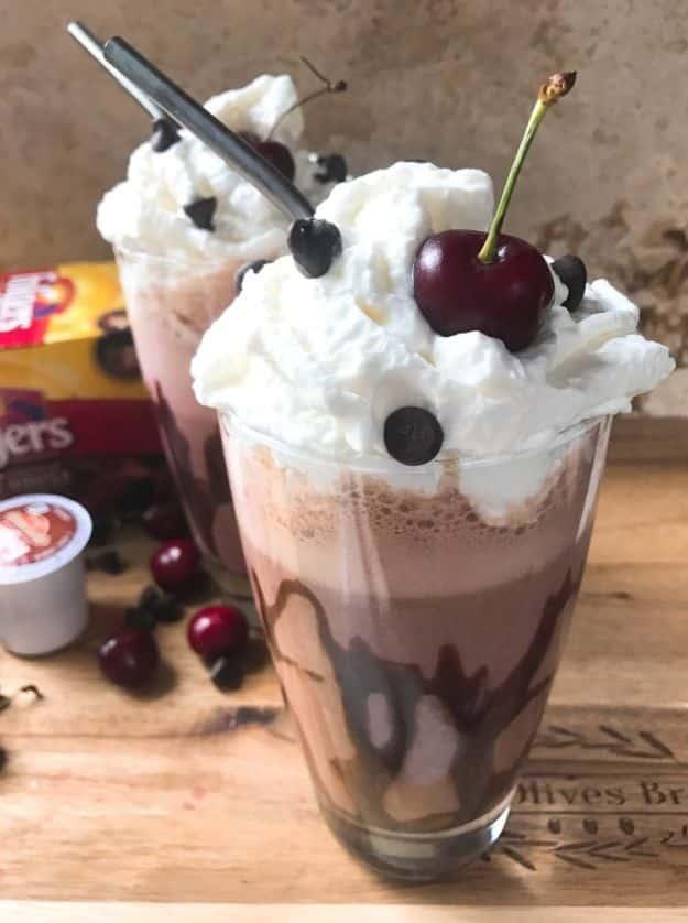 Frozen black forest mocha in a chocolate drizzled glass topped with whipped cream and a cherry, cherries beside