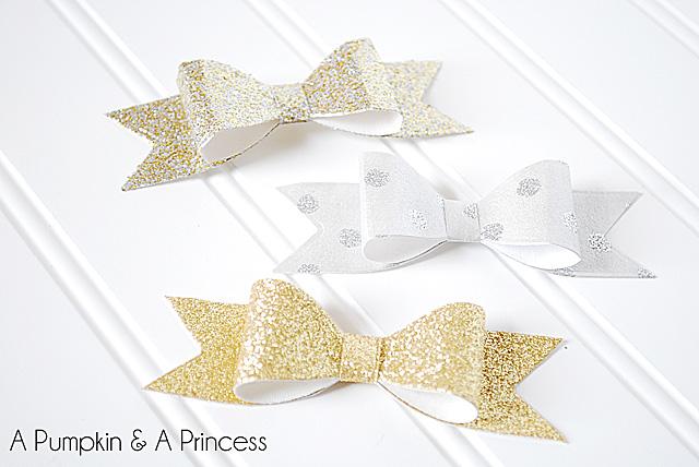 Three handmade paper bows in gold glitter, silver glitter and dotted white on a white painted background