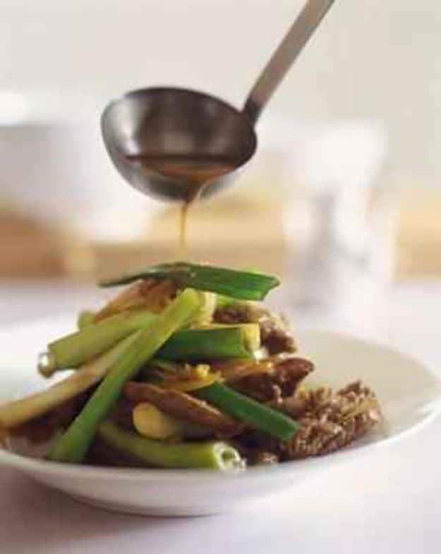 Kylie Kwong stir fried beef with spring onions in a white bowl as a dark glossy sauce is ladled over it