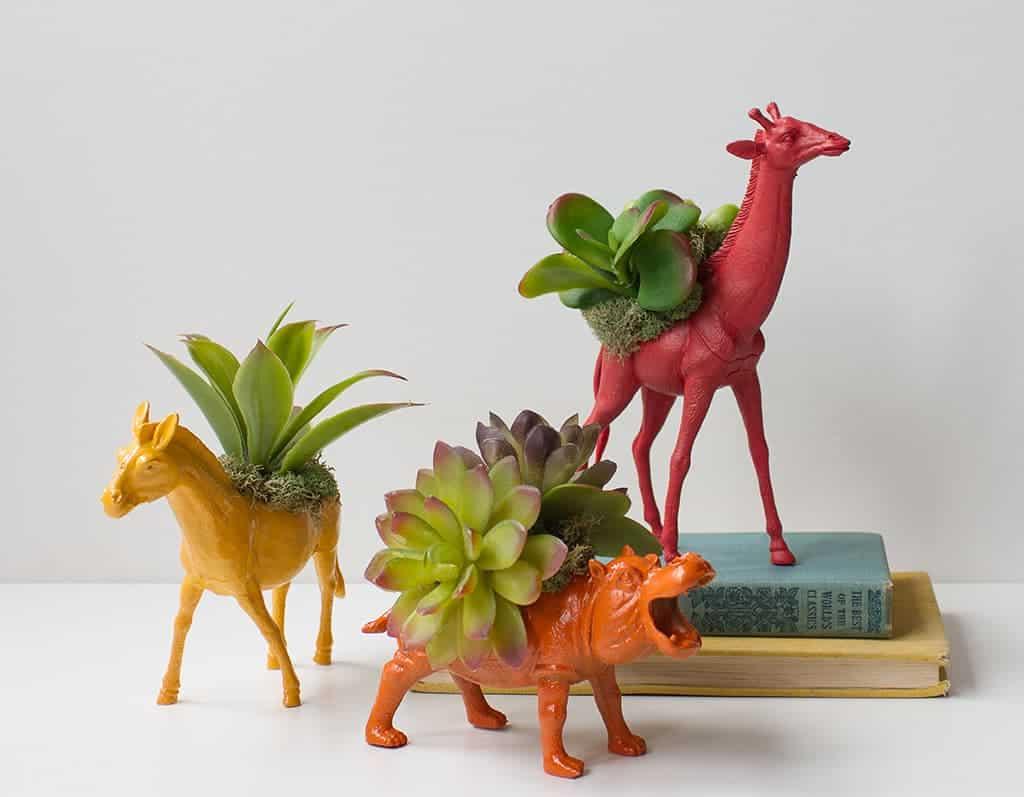 A yellow horse, an orange hippo and a red giraffe toy planter with succulents growing from their painted backs