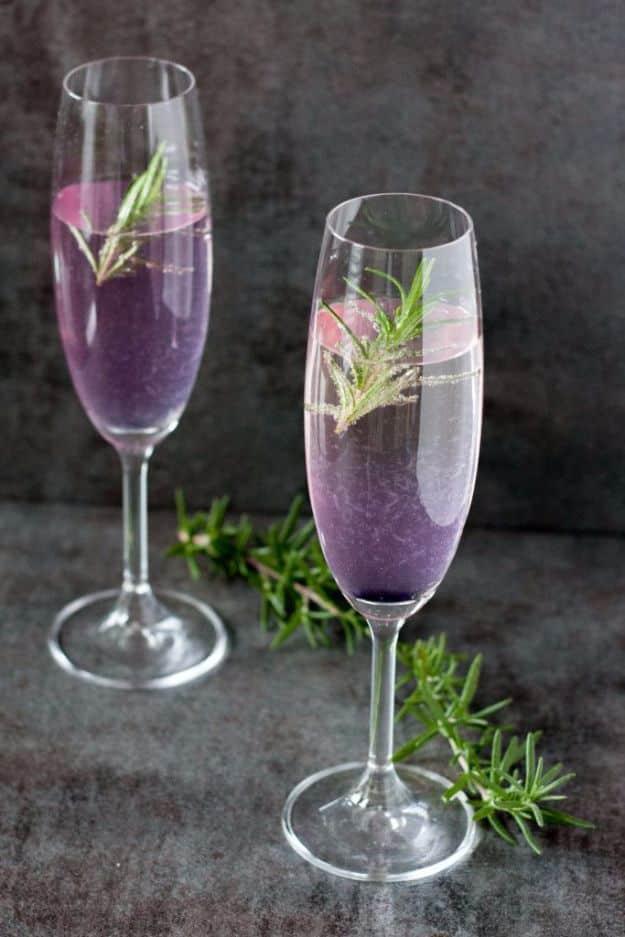Two champagne flutes of pale purple Rosemary 75 cocktail with fresh rosemary sprigs standing in the glasses