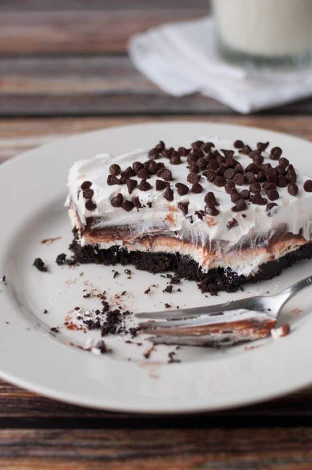 Chocolate lasagna slice on a white plate showing Oreo, cream cheese and pudding layers under mini chips