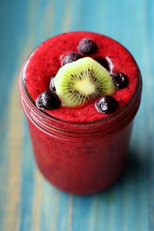 Thick deep red berry kiwi smoothie in a jar topped with a kiwi slice and blueberries on a turquoise painted wood table