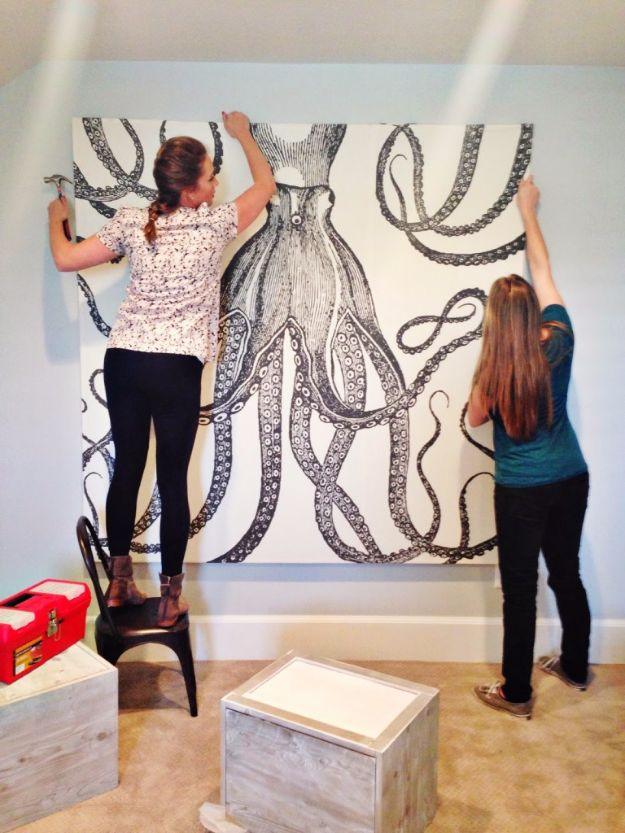 Two women lifting a very large canvas printed with a black and white octopus made from a shower curtain onto a wall