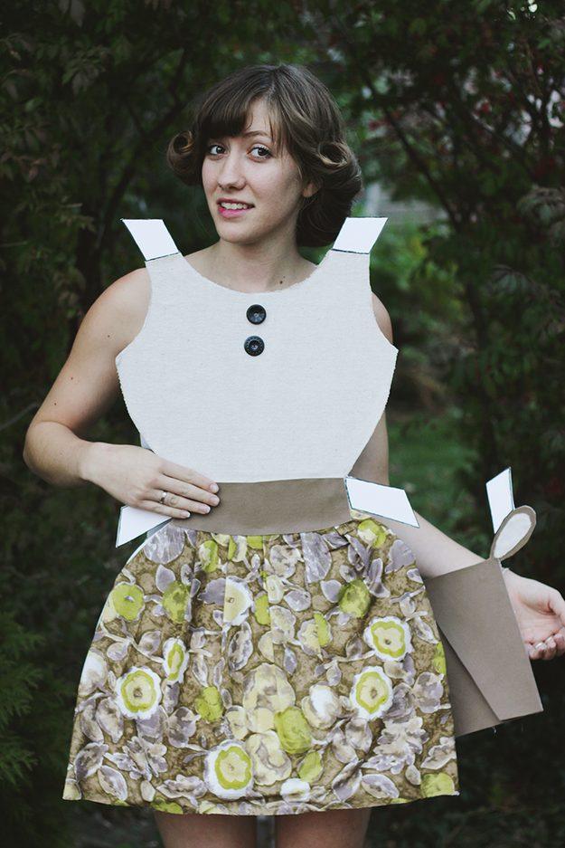 Woman wearing a foam-board paper doll dress with a floral skirt, large buttons, white tabs and a matching handbag