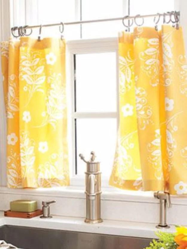 Yellow and white floral cafe curtains hanging on a rod across a kitchen window above a sink and faucet