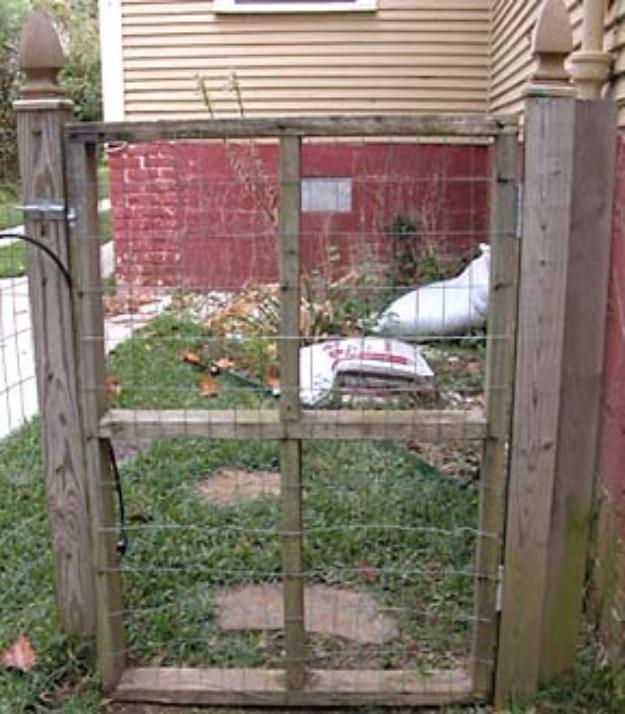 Basic mesh fence, a wire mesh gate in a rough wooden frame set between weathered posts with a grass yard behind it