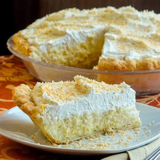 Whole old fashioned coconut cream pie with a tall whipped cream top and one cut slice on a plate beside it