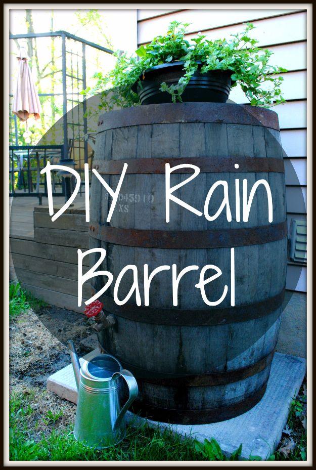 DIY rain barrel made from an old whiskey barrel beside a house with ferns planted on top and a watering can below