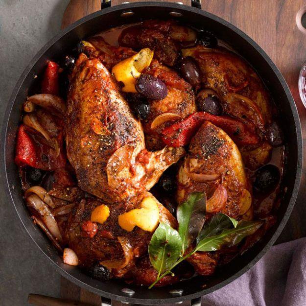 Chicken braised in a dutch oven with olives, strips of orange zest and roasted red peppers in a red wine sauce