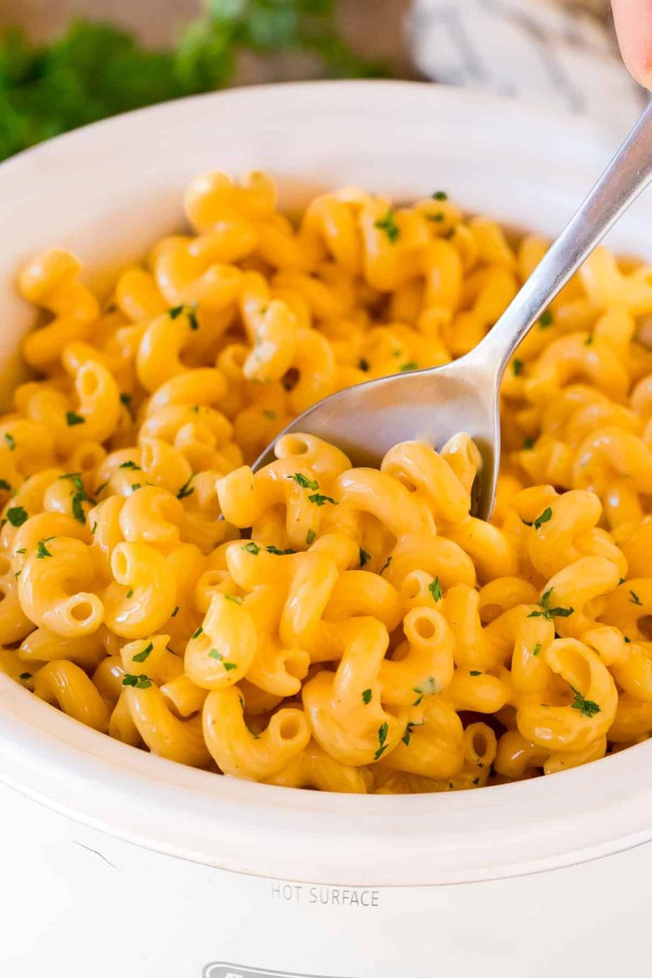 Creamy cavatappi macaroni and cheese in a white slow cooker with parsley and a serving spoon for holiday meals