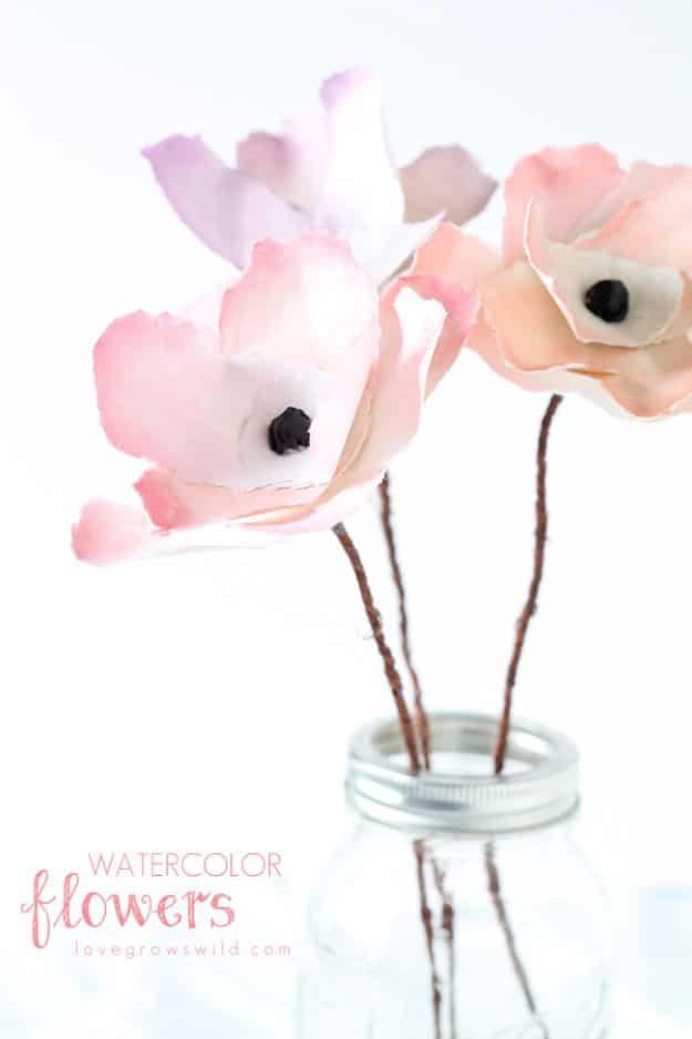 Watercolor flowers, three pale pink watercolor paper flowers with black centers on twig stems in a glass jar