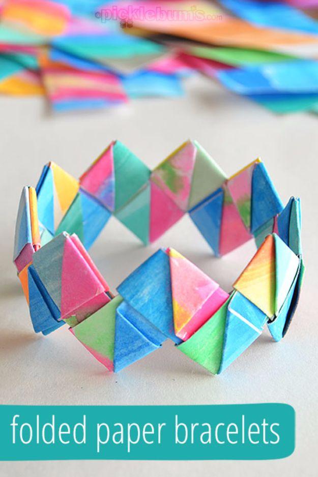 Bracelet of interlocking folded paper triangles in pink, blue, green and yellow, with cut paper strips behind it