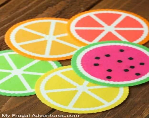Five perler bead coasters made as lemon, lime, orange and watermelon slices, overlapping on a dark wooden table