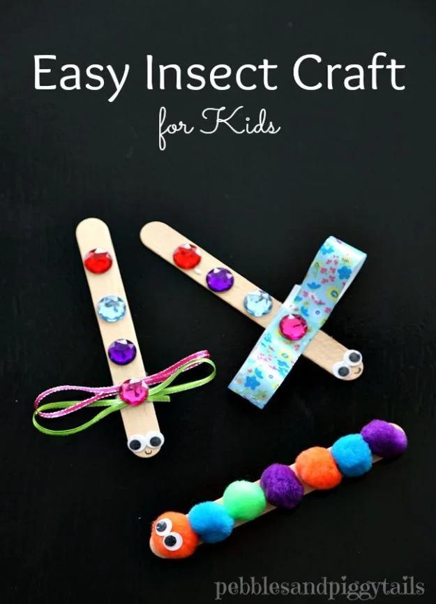 A craft stick dragonfly with ribbon wings and gems beside a craft stick caterpillar covered in colored pom poms
