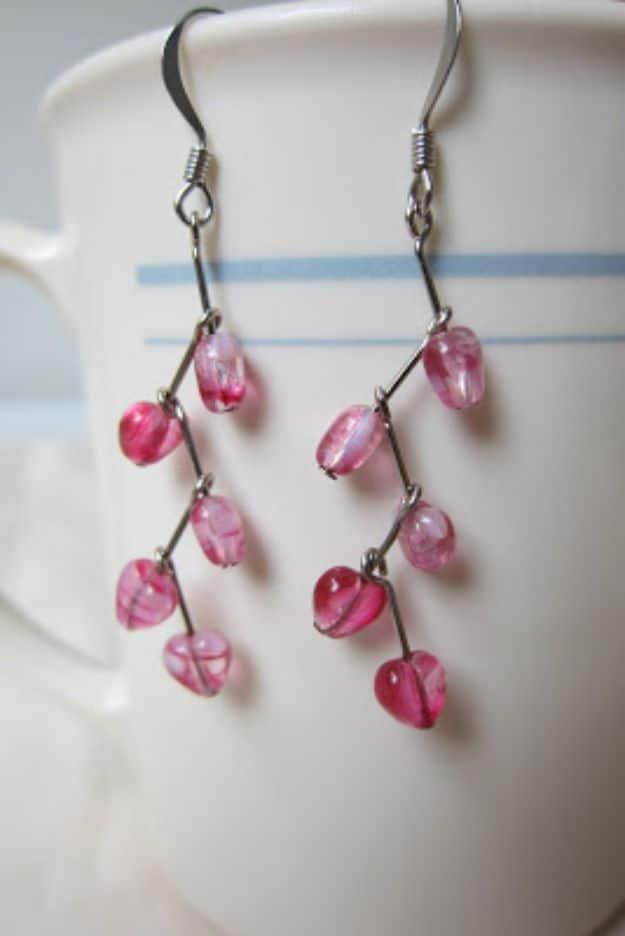 Dangly earrings made from pink glass heart beads linked on silver wires, hanging against a white striped coffee mug