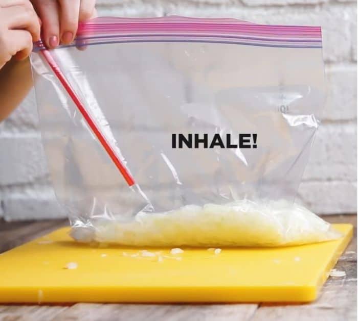 A zip-top bag of prepped Thanksgiving vegetables being vacuum sealed with a drinking straw, an easy make ahead hack