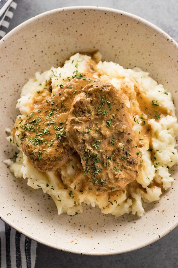 Slow cooker pork chop served over a mound of mashed potatoes and covered in thick brown gravy with parsley