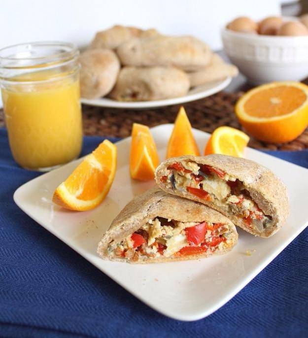 Homemade breakfast hot pocket cut in half showing egg, sausage and red pepper filling with orange slices