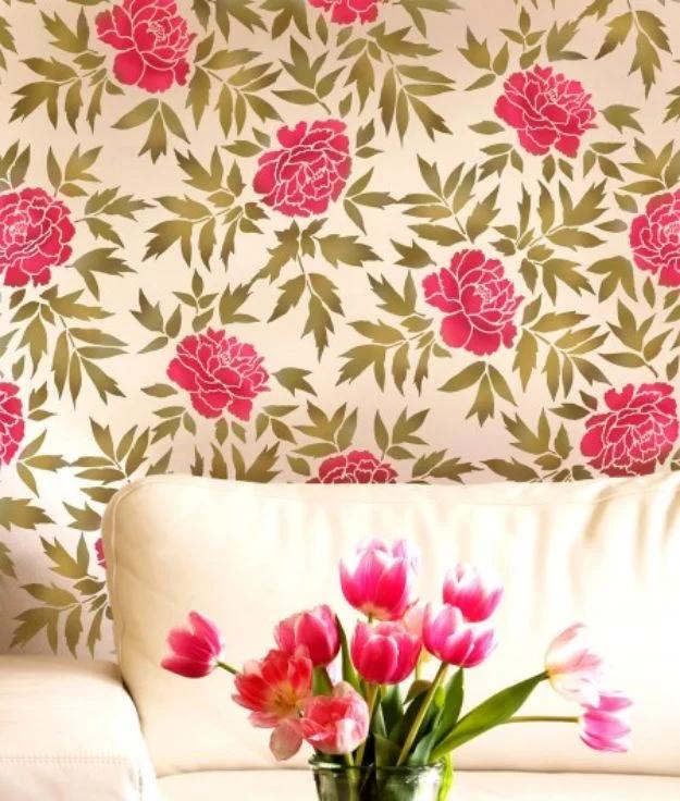 Wall stenciled with bright pink peonies and gold green leaves behind a cream sofa and a jar of pink tulips