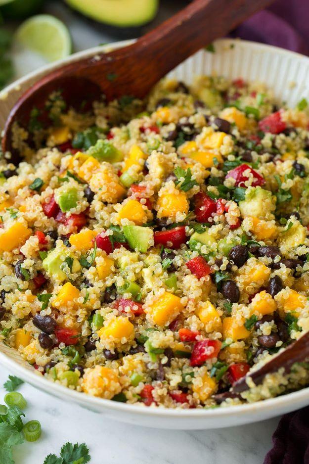 Mango black bean and avocado quinoa salad in a white bowl with diced mango, peppers and a wooden spoon