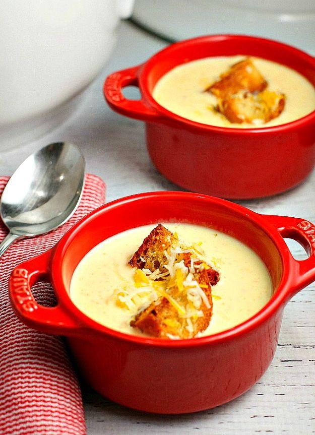 Cheese soup served in two small red crocks topped with croutons, on a red and white striped tea towel