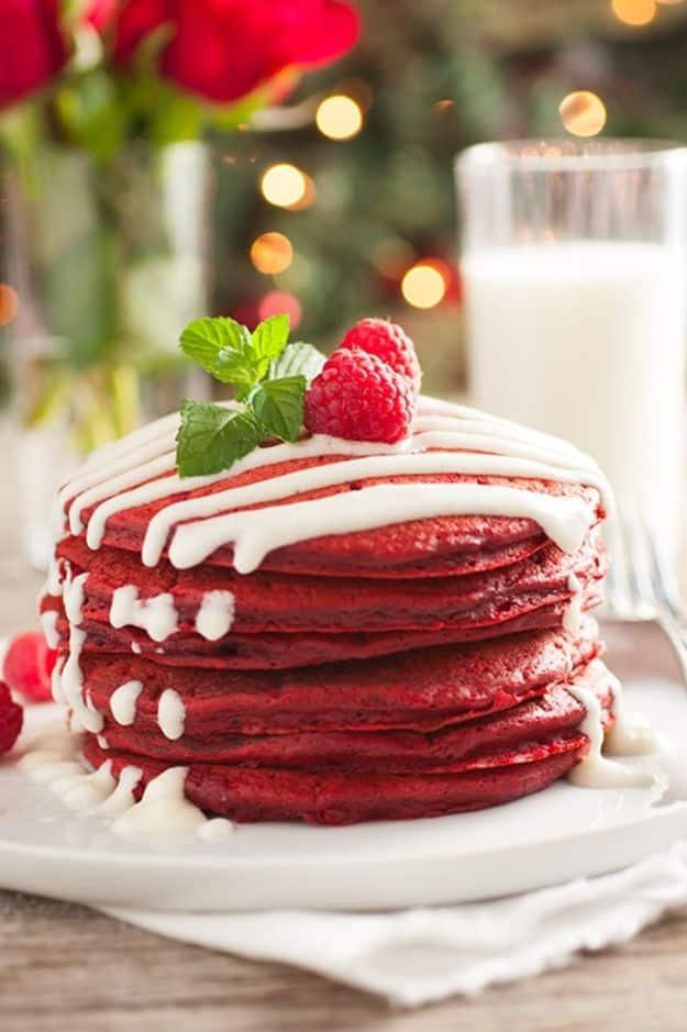 Red velvet pancakes stacked tall with white cream cheese glaze dripping down, raspberries and mint on top