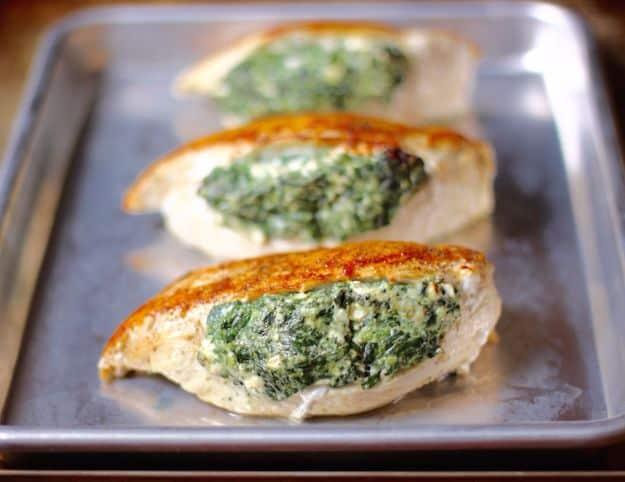 Three spinach and feta stuffed chicken breasts browned on a metal sheet pan fresh out of the hot oven