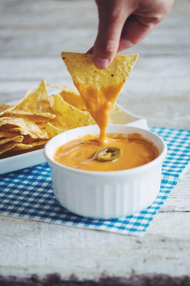 Vegan nacho cheese, a smooth orange sauce in a white dish being scooped up with a tortilla chip by hand