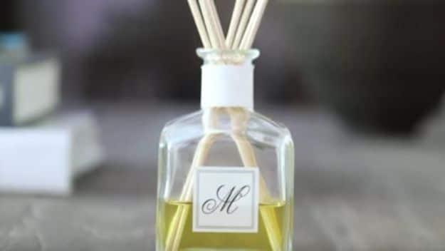 Glass reed diffuser bottle with a monogram label and a bunch of natural reeds standing on a dark stone countertop