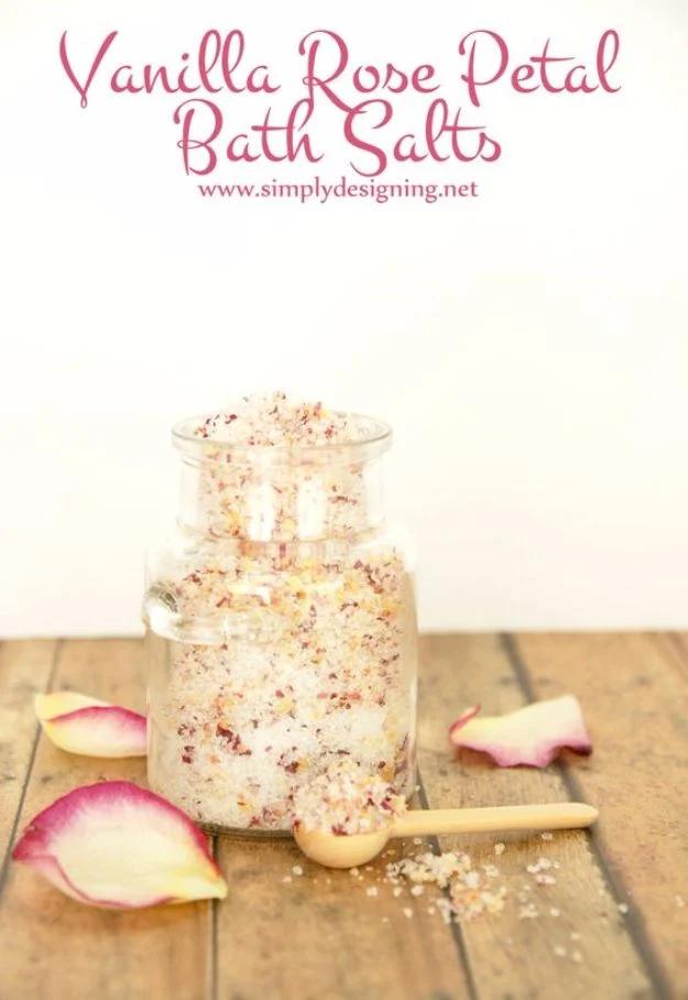 Vanilla rose petal bath salts, a glass jar of coarse white salt flecked with petals, a wooden spoon and loose petals