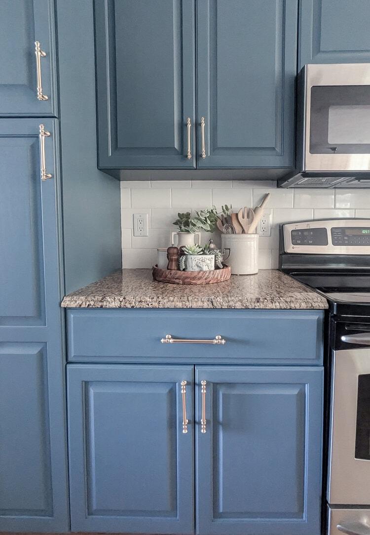 Kitchen cabinets repainted a muted slate blue with long champagne bronze bar pulls and a speckled granite counter