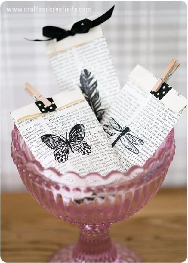 Book page gift bags folded from old dictionary pages with butterfly stamps and clothes pins, in a pink glass bowl