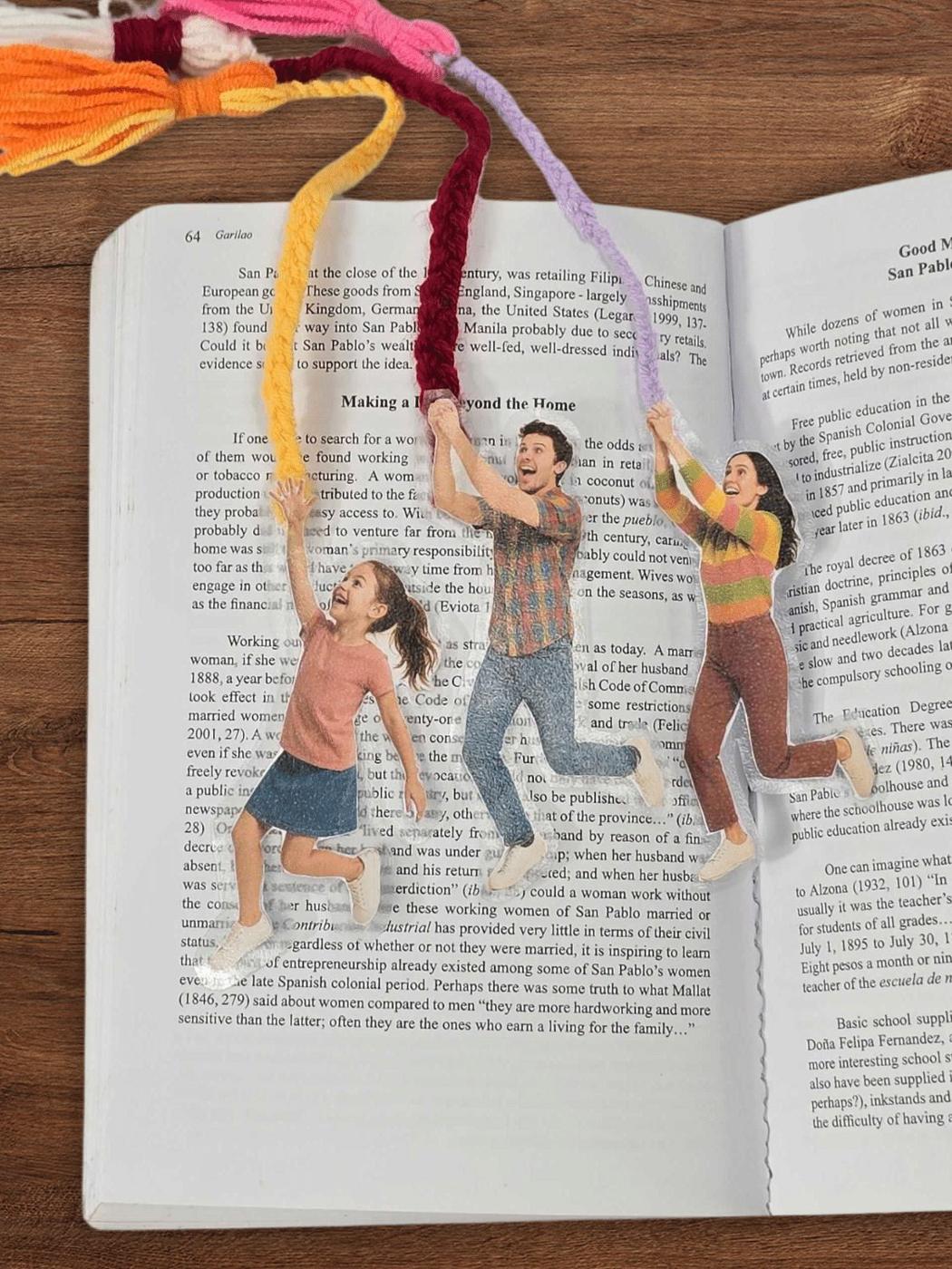 Bookmarks made from cutout photos of people holding colorful tassels in their hands, laid across an open book