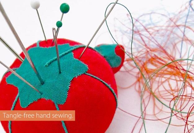 A red tomato pincushion stuck full of pins beside a loose tangle of colored thread on a white surface