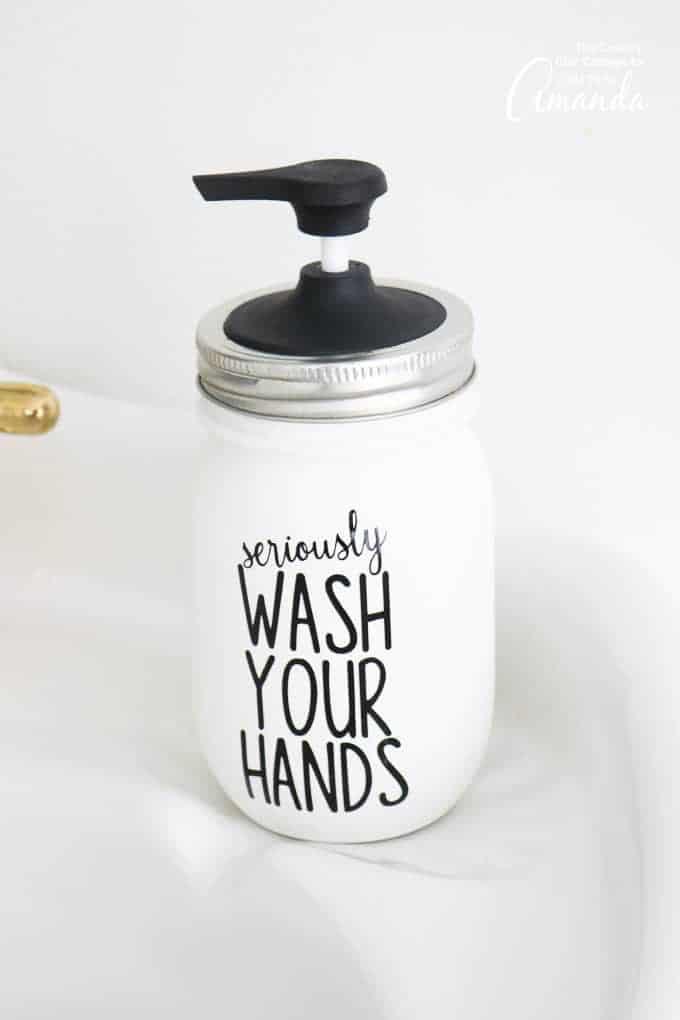 White painted mason jar soap dispenser with a black wash your hands decal and a black pump lid on a bathroom counter