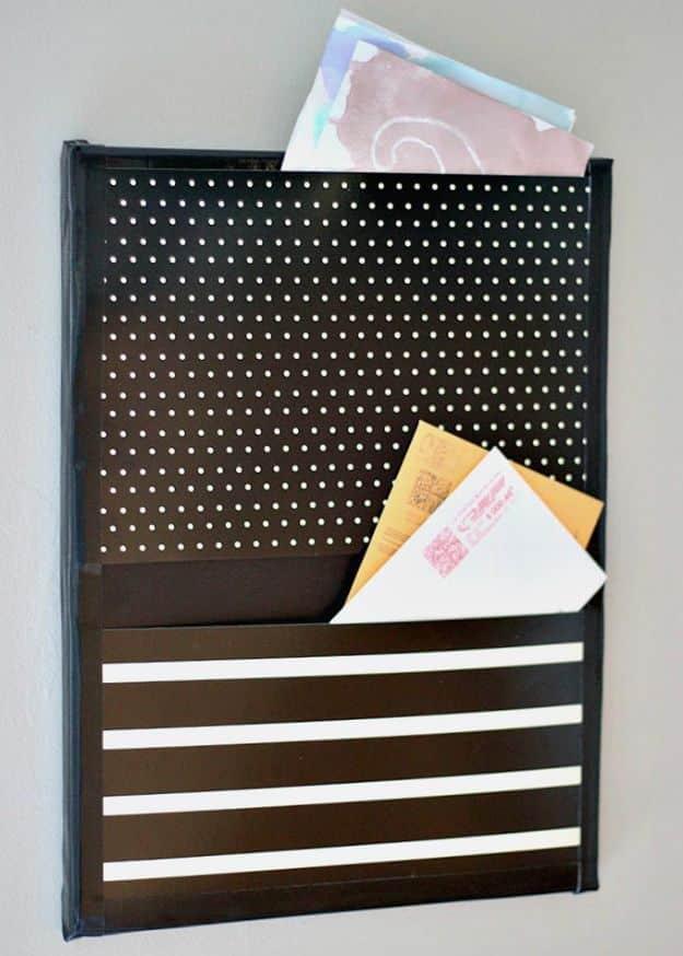 Dark canvas wall pocket with a dotted upper panel and striped lower panel, holding envelopes and papers on a gray wall