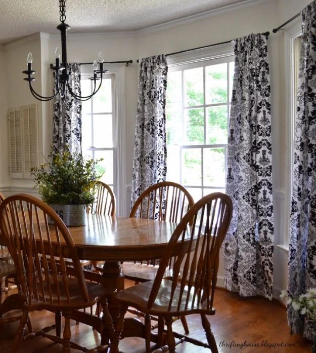 DIY curtain panels in black and white damask hanging at a bay window above a wooden dining table and windsor chairs