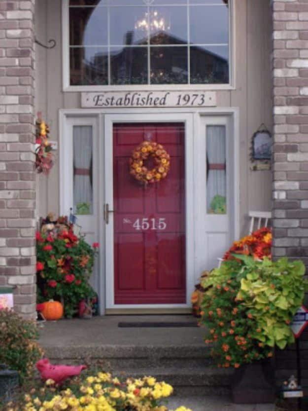 White house numbers applied to the glass of a storm door above a burgundy front door on a brick porch