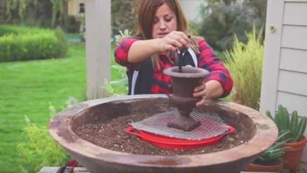 A woman setting a small water fountain into a wide planter of soil before it is filled in with succulents