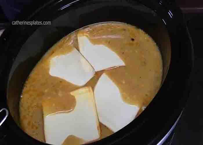 Adding the cheese to the slow cooker with the chicken breasts